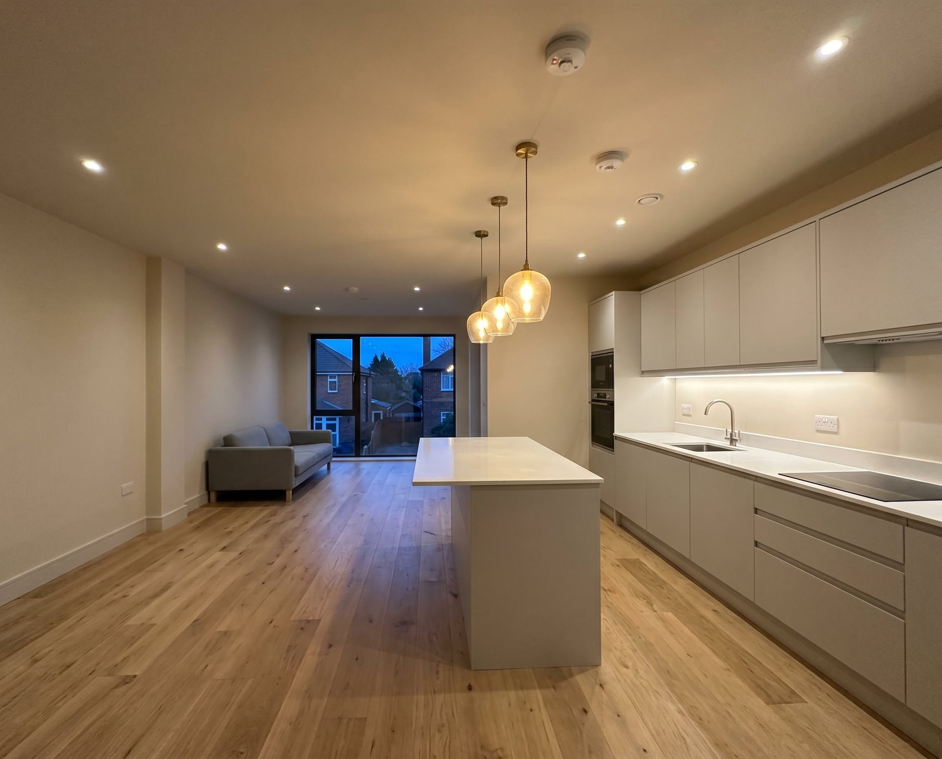 Modern kitchen with white cabinetry, white island, wooden floors, and pendant lighting overlooking a living room and city skyline