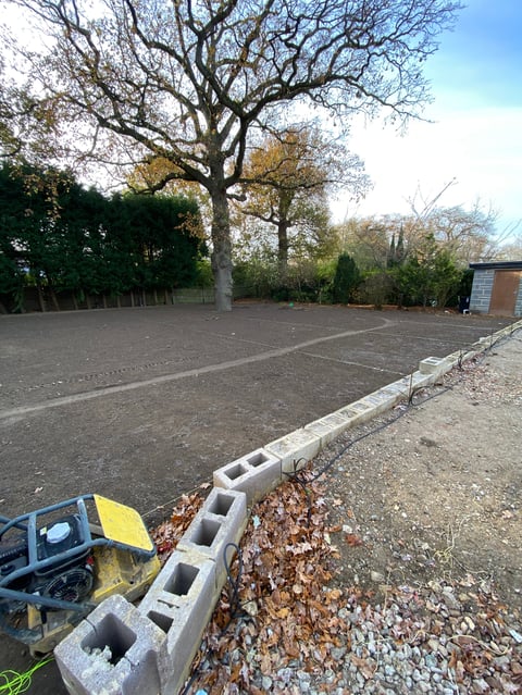 Construction site with concrete foundation, cinder blocks lining the edge, and a large bare tree in the background