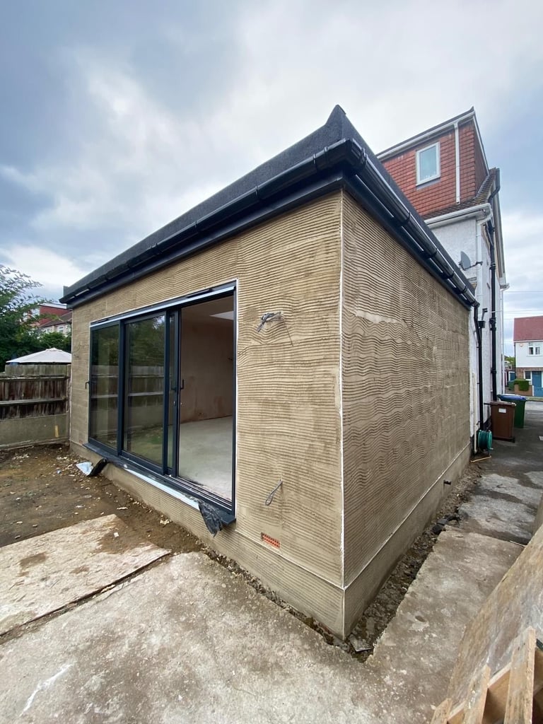 Modern garden studio with wooden walls, black roof, and glass sliding doors attached to brick house