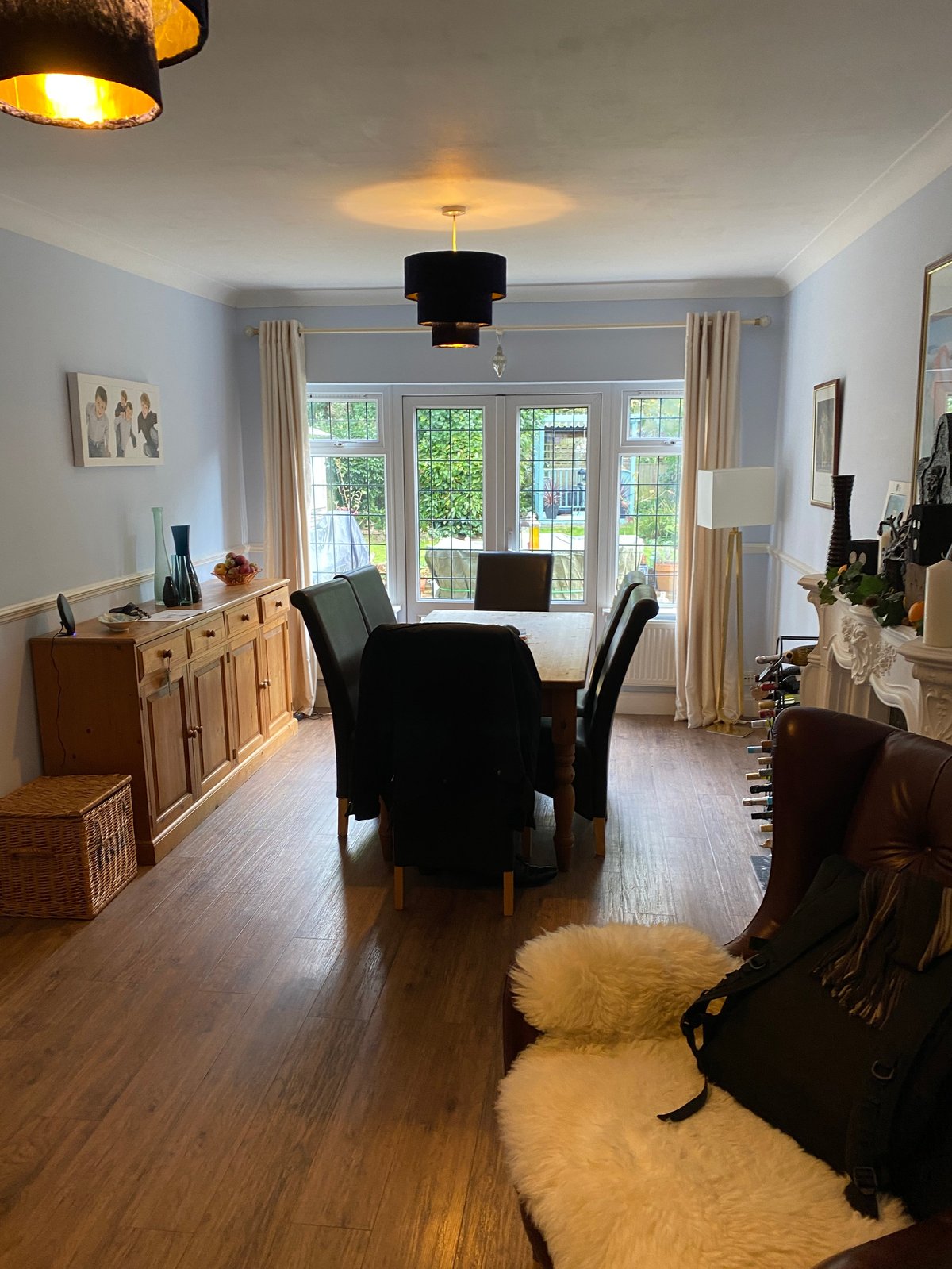 Bright living room with light blue walls, wooden flooring, black dining table, leather armchairs, and patio doors overlooking greenery