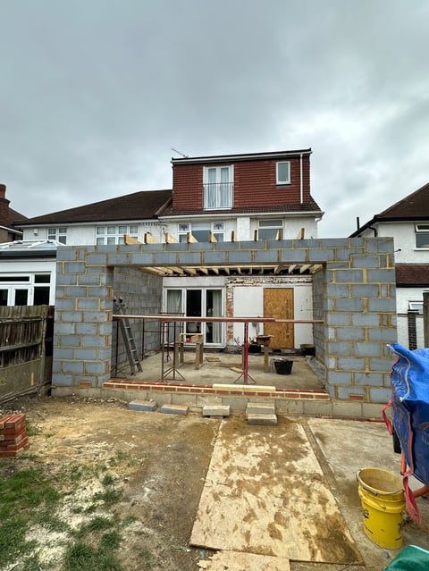 Brick extension structure under construction in residential backyard with exposed interior, adjacent houses visible in background