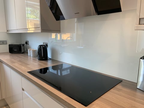Modern kitchen with white cabinetry, black induction cooktop, white glass backsplash, and stainless steel range hood