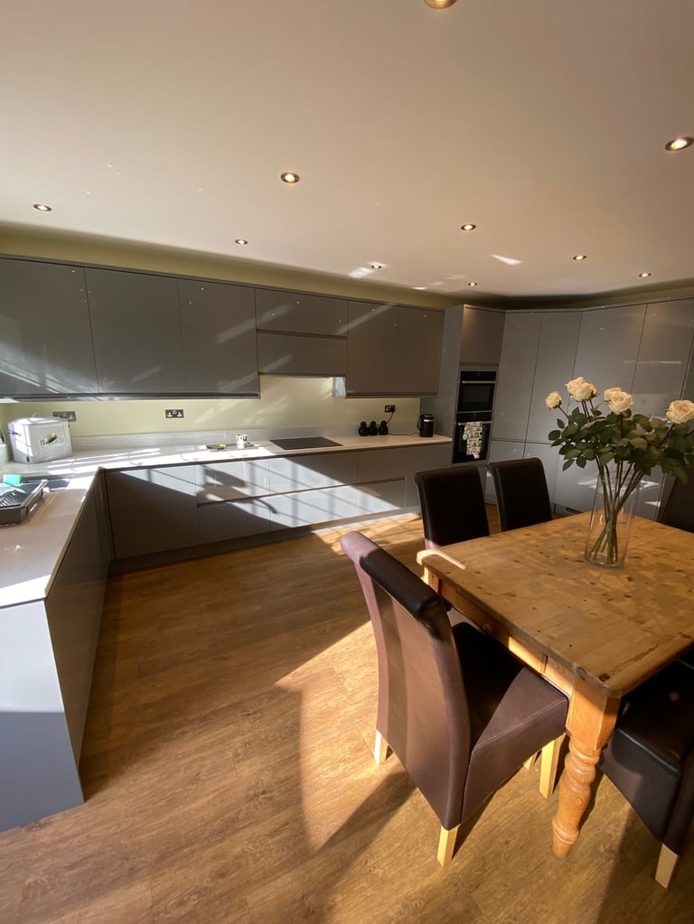 Modern kitchen and dining area with wooden table, black chairs, and gray cabinetry under warm lighting
