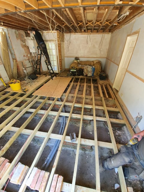 Unfinished basement room under construction with exposed wooden floor joists, framing, and drywall in progress