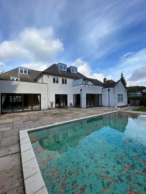 Modern white house with slate roof and swimming pool under blue sky with white clouds