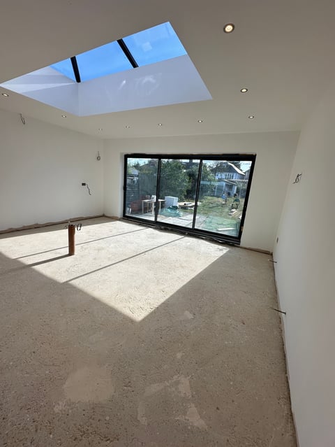 Empty room with concrete floor, white walls, triple sliding glass doors, and blue skylights with black frames overhead