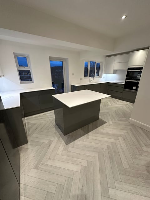 Modern kitchen interior with black cabinetry, white countertop island, herringbone wood flooring, and built-in appliances