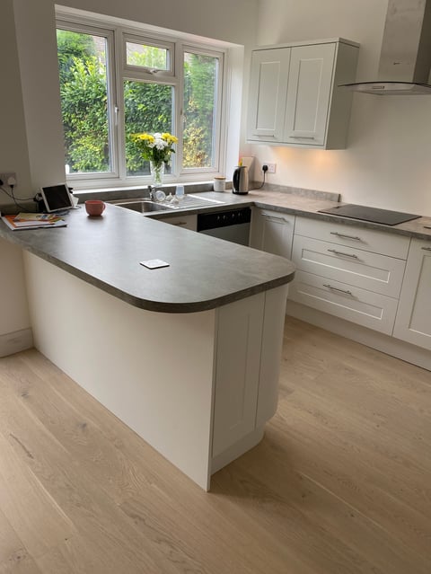 Modern white kitchen with curved island countertop, built-in appliances, and large windows overlooking greenery