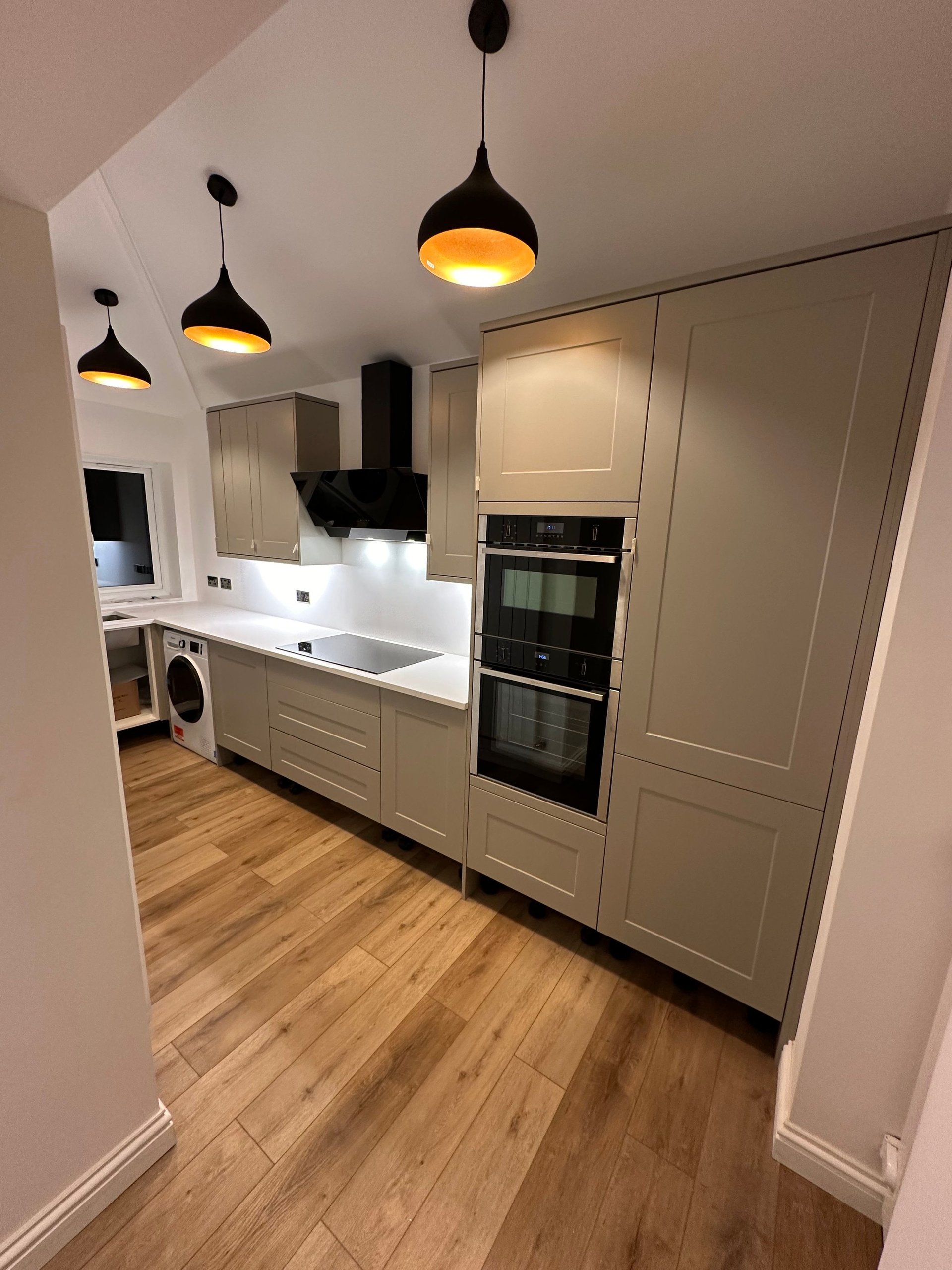 Modern kitchen with cream cabinetry, white countertops, double built-in ovens, black pendant lights, and wooden flooring
