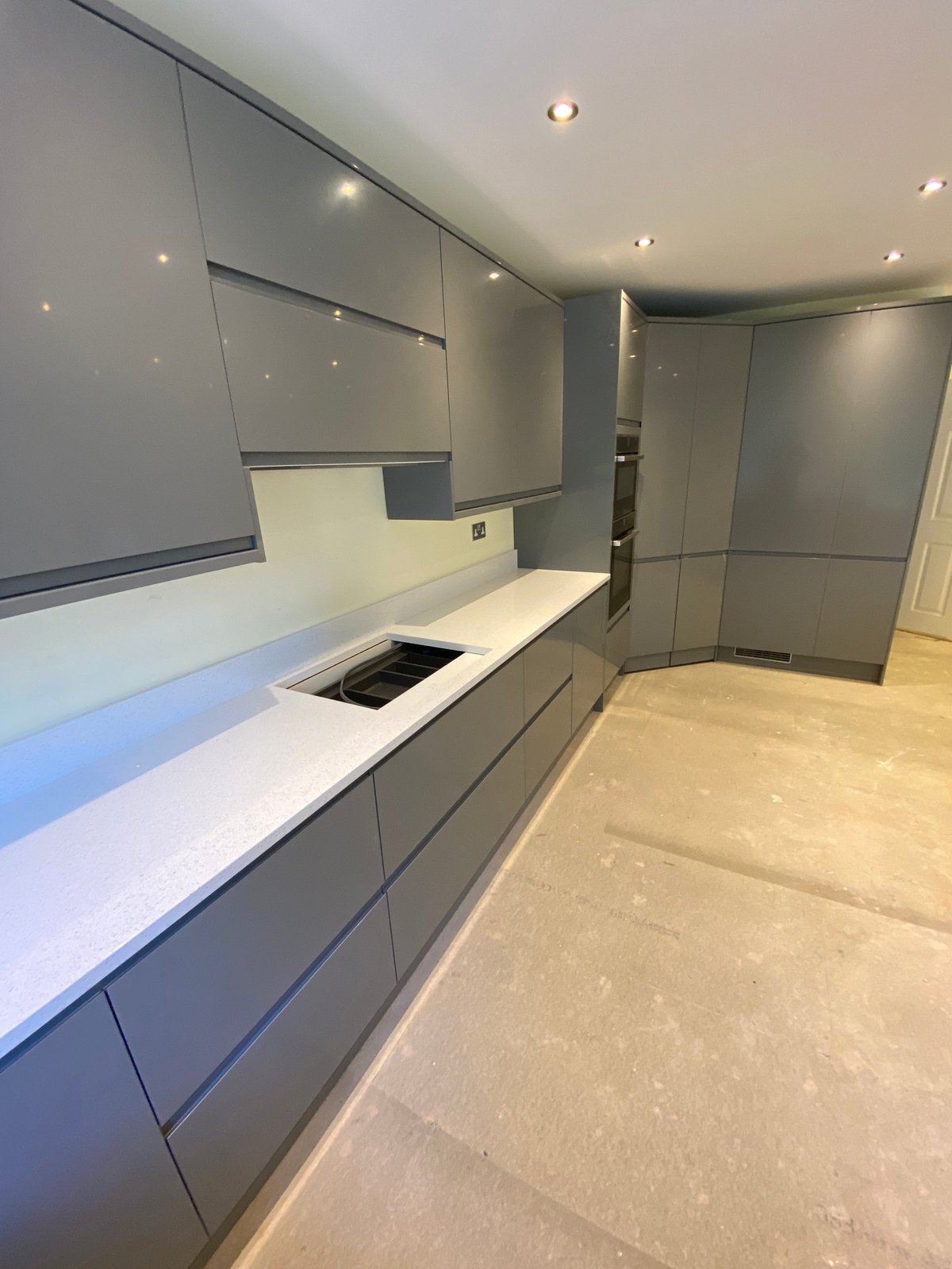 Modern minimalist kitchen with gray cabinetry, white countertop, induction cooktop, and recessed ceiling lights