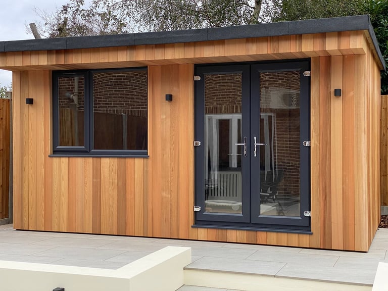 Modern wooden garden studio or studio pod with dark framed windows and double doors on a concrete platform