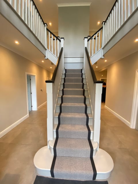 Modern symmetrical staircase with gray carpeted steps, white railings, and black trim, viewed from above with hallways on both sides