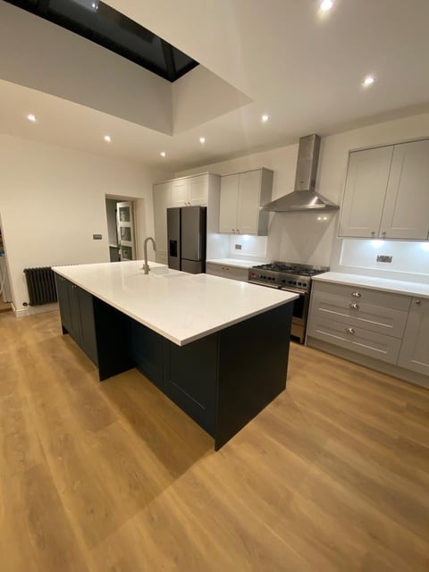 Modern kitchen with black and white cabinetry, white countertops, central island, stainless steel appliances, and wooden flooring